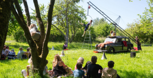 A group of people sitting in the grass watching aerial circus performance rigged to a black taxi cab